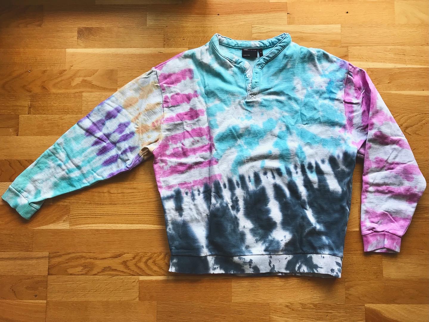 Assorted paried tye died shirts and sweat shirts with different motifs and black, turquoise, violet, pink and orange colours.